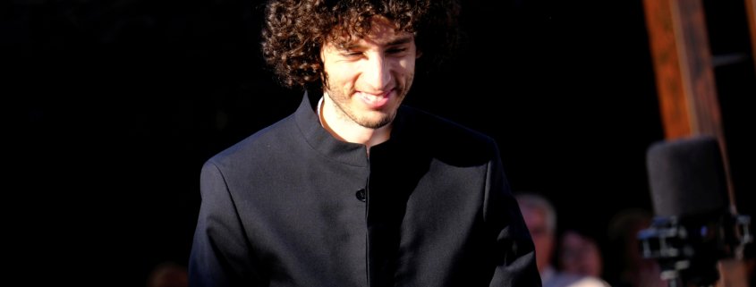 Tami Daniel Rueda-Blanco, director asociado de la Orquesta Filarmónica de Medellín, sonríe mientras saluda al público durante un evento al aire libre.